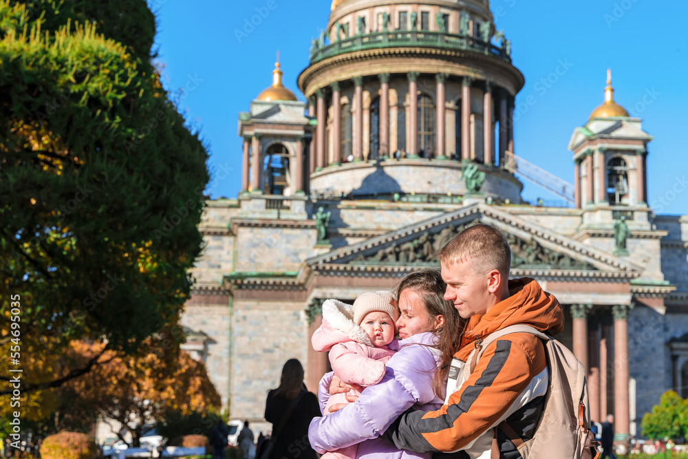 A young family mother and father hold a little baby against the background of St. Isaac's Cathedral in St. Petersburg