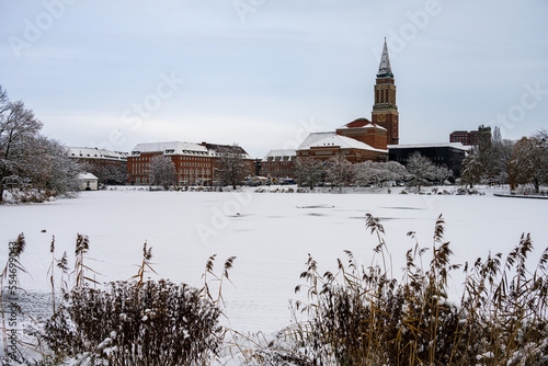 Zugefrorener und Schnee bedeckter  See in der Innenstadt Kiels mit Blick auf das Rathaus und des Opernhaus im Dezember