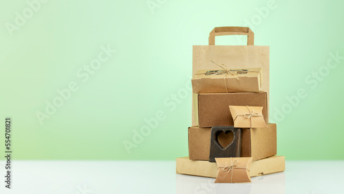 Eco friendly shopping and delivery service. Craft cardboard gift boxes, paper bag and wooden heart on green background with copy space. Zero Waste, plastic free, eco packaging concept. Front view