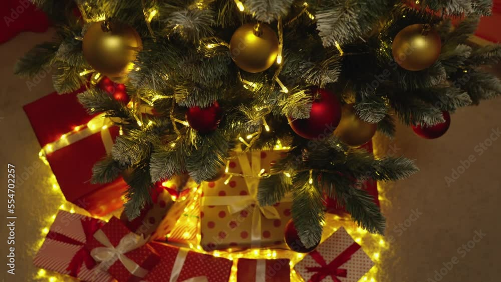 New Year's holiday atmosphere, winter fairy tale and Christmas spirit at home. Gift red packages with ribbons under a green tree. Slow motion. Decorated Christmas tree with lights, balls and presents. New Year's holiday atmosphere, winter fairy tale and Christmas spirit at home. Gift red packages with ribbons under a green tree. Slow motion. Decorated Christmas tree with lights, balls and presents.