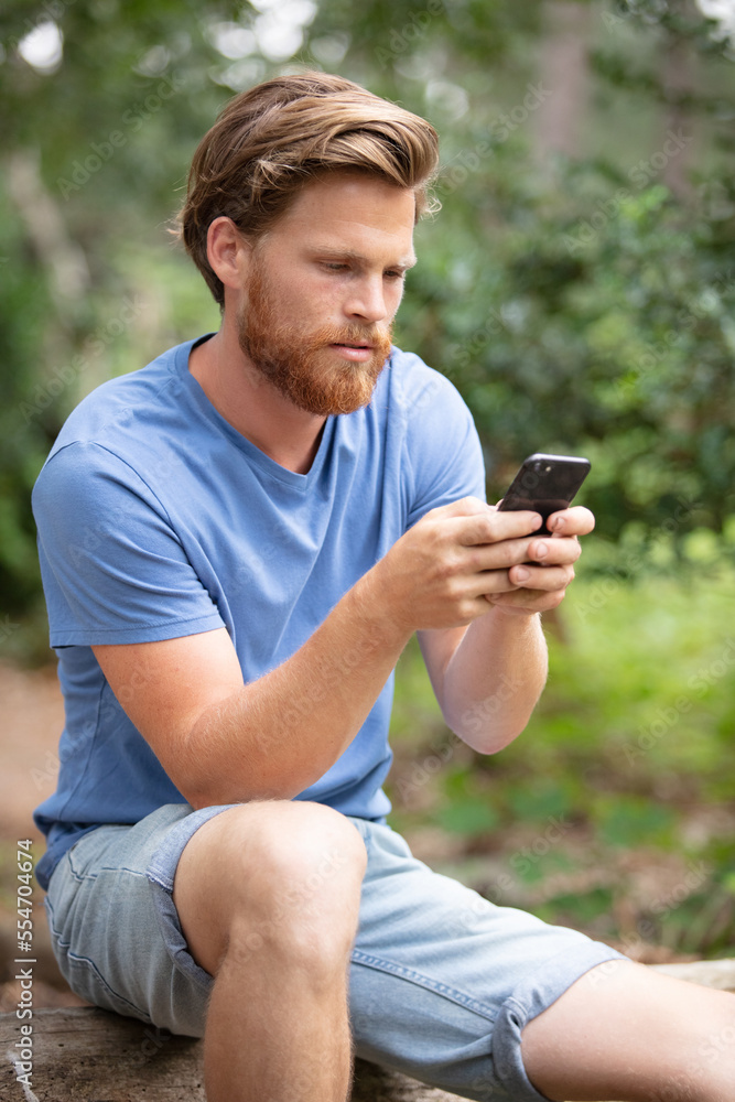 attractive young man sitting in the park using mobile phone attractive young man sitting in the park using mobile phone