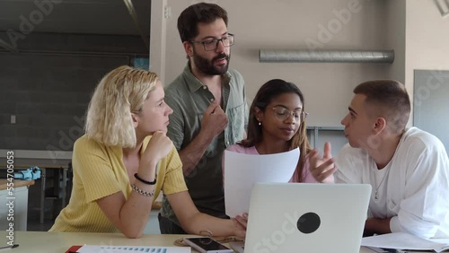 Male teacher explaining in class to a group of diverse students in a classroom with laptops