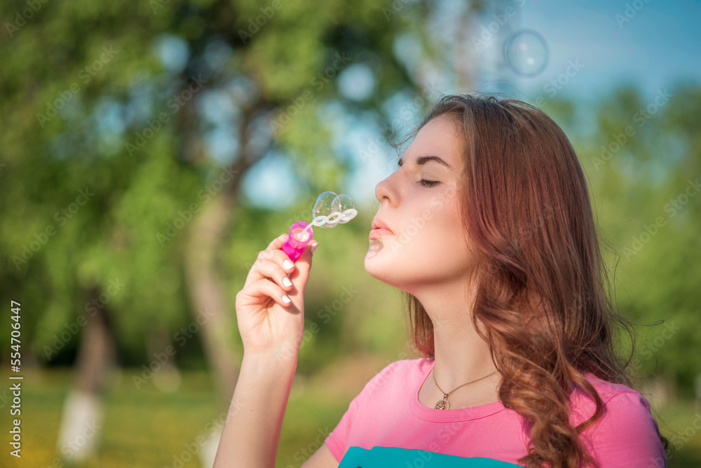 A young beautiful girl blows soap bubbles in a summer park. A young beautiful girl blows soap bubbles in a summer park.