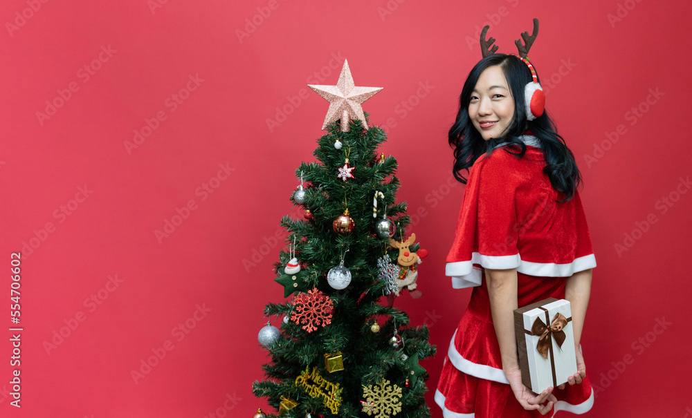 Beautiful asia woman in red santy costume holding gift box Isolated red background and christmas tree. Beautiful asia woman in red santy costume holding gift box Isolated red background and christmas tree.