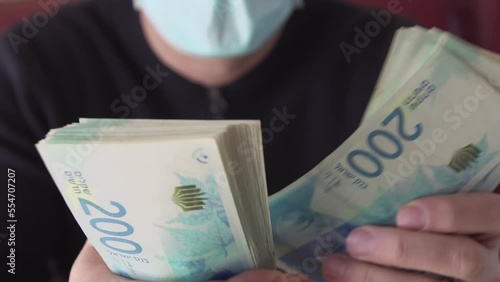 Counting cash Sheqel Israel currency paper 200 shekel nominal banknotes. Closeup of israeli man in face mask