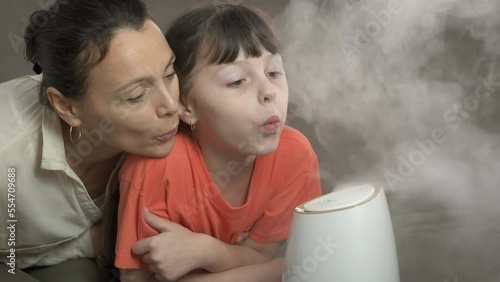 Home humidifier. Water mist by working humidifier. A mother with her small daugher enjoy the water mist from air purifier in the room. photo