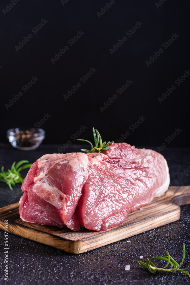 Raw pork ham, salt and rosemary on a cutting board on a dark background. Vertical view Raw pork ham, salt and rosemary on a cutting board on a dark background. Vertical view