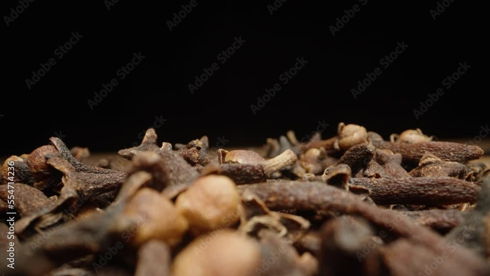The nutmeg is lying on a handful of cloves, I examine it and take it away. Black background, close-up. The nutmeg is lying on a handful of cloves, I examine it and take it away. Black background, close-up.