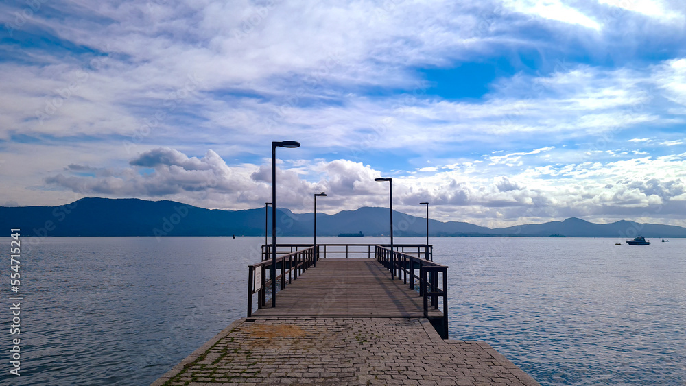 Empty wooden beach deck with pole, sunny cloudy day and mountains
