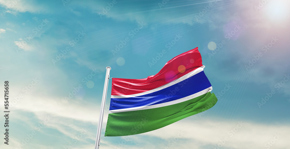 waving flag of The Gambia in blue sky. the symbol of the state on wavy ...