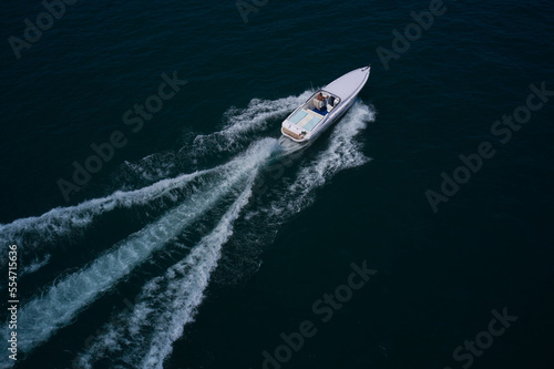 Speedboat with a man moving diagonally. White boat fast movement on dark water, white trail on the water.