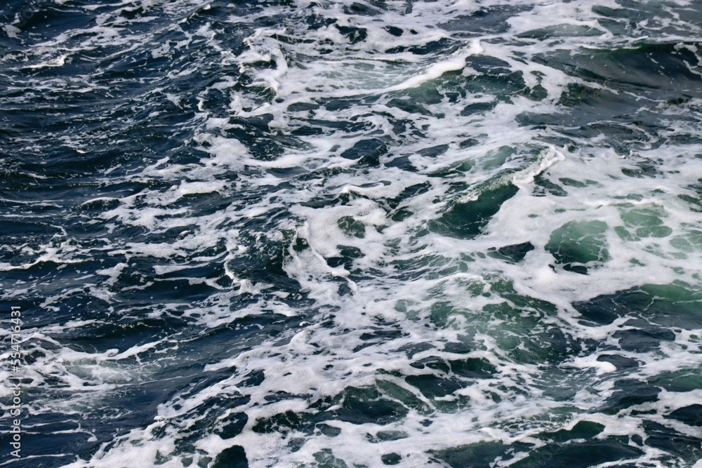 Stern waves with white foam tips on greyish blue sea water, photo taken from aboard ship. Selective focus Stern waves with white foam tips on greyish blue sea water, photo taken from aboard ship. Selective focus