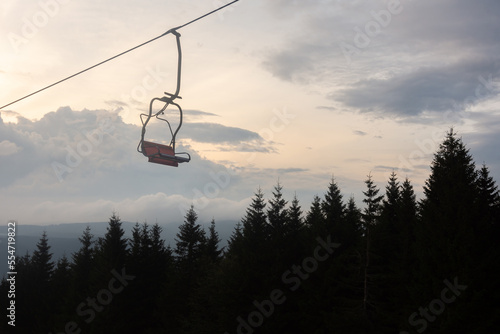 Chair lift in foreground, forrest and cloudy sky in background at evening.