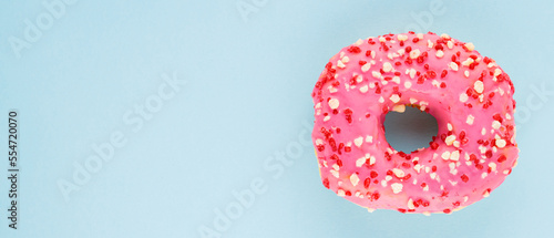 Pink sweet donut with pink sprinkles. Delicious glazed donut on blue background. Top view. Copy space