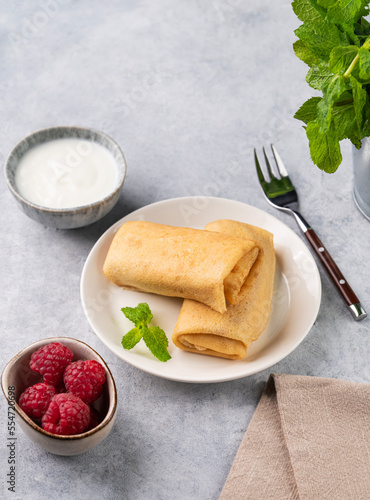 Homemade roll crepes with raspberry and sour cream on a plate on a light background with fresh mint.