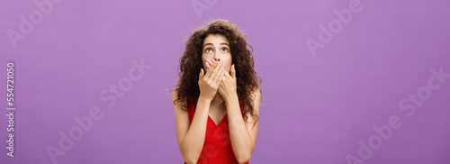 Woman being shocked and stunned seing guy about fall down from tree gasping feeling nervous covering opened from amazement mouth looking up standing intense over purple background in evening red dress photo