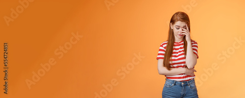 Annoyed redhead woman fed up listening stupid nonsense, close eyes tired, make face palm embarrassed uninterested, feel uneasy distressed, exhausted useless argument, irritated orange background photo