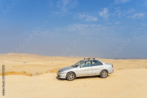 Gray Egyptian car beaten in many places, with the desert and the pyramids in the background.