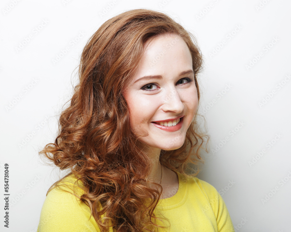 Pretty young woman with curly hair and cute smile poses alone against white background.
