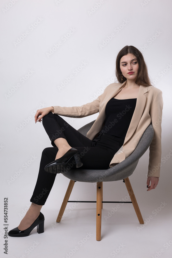 Portrait of a young brunette with long hair in the studio. Cute girl sitting on a chair on a white background. Portrait of a young brunette with long hair in the studio. Cute girl sitting on a chair on a white background.