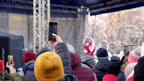 A crowd admires a street concert by a soloist dressed as a snow maiden on winter Christmas Eve in Krakow. Fans record the performance of the singer on smartphones on the street on a frosty day