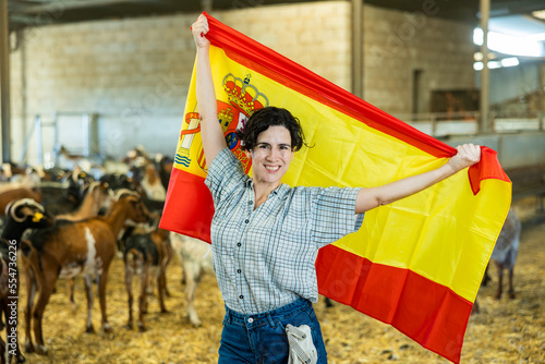 Portrait of happy female farmer with spanish flag in their hands in goat pen at farm