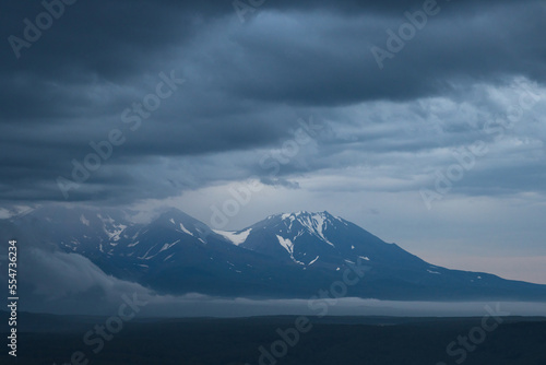 Beautiful evening landscape. View of the volcanoes at dusk. Overcast weather. Low clouds. The majestic nature of the Kamchatka Peninsula. Travel and tourism in Siberia and the Russian Far East. Russia