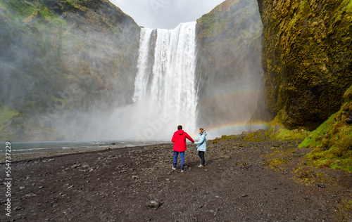 man and woman in love next to the waterfall in iceland