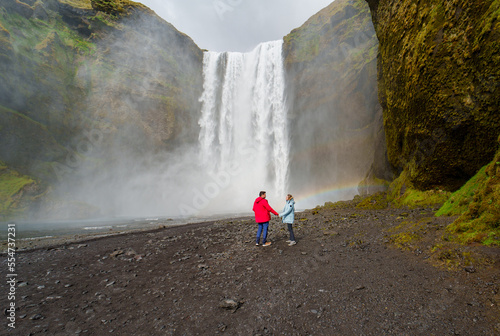 man and woman in love next to the waterfall in iceland
