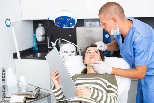 Male beautician in gloves examining face skin of young woman before procedure at cosmetology clinic