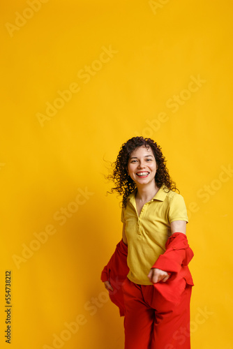 Curly cute girl laughs and jumps. Studio portrait of a woman on a bright yellow background. Happy smiling young female dancing in bright clothes