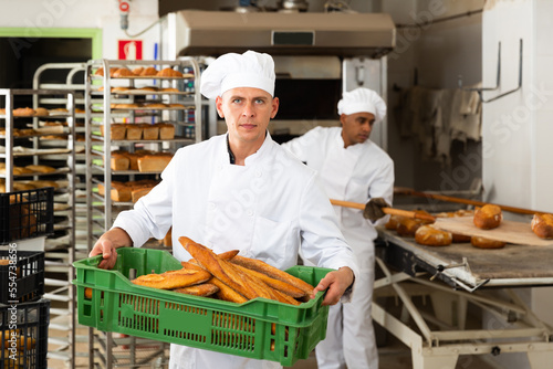 Portrait of focused male chef standing in bakery kitchen with fresh bread in crate