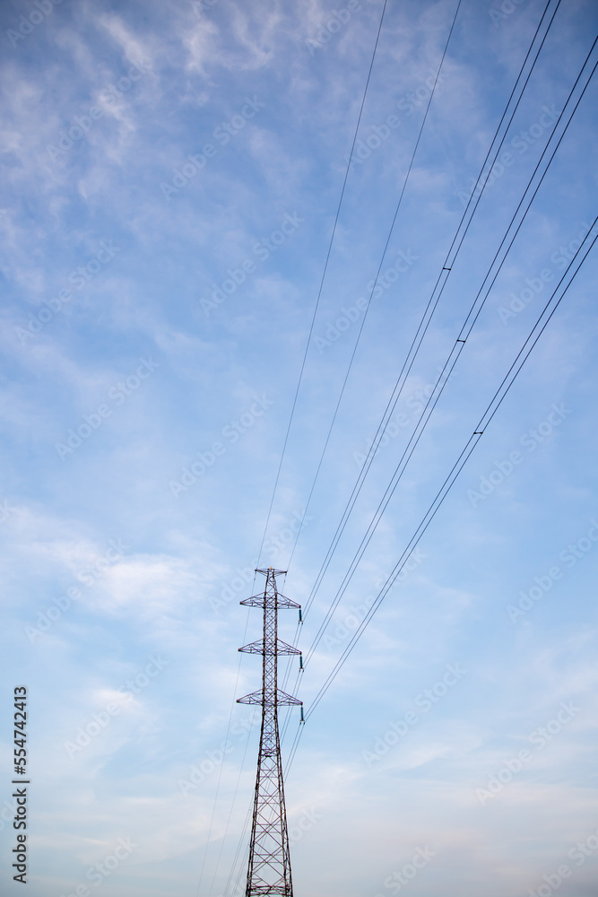 Power lines and electric tower with blue sky and clouds on background.