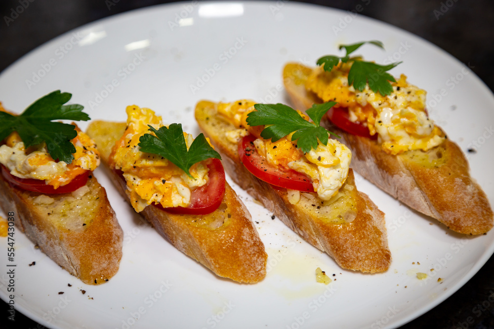 Bread with scrambled egg over ripe tomato and decorated with parsley leaf and black pepper