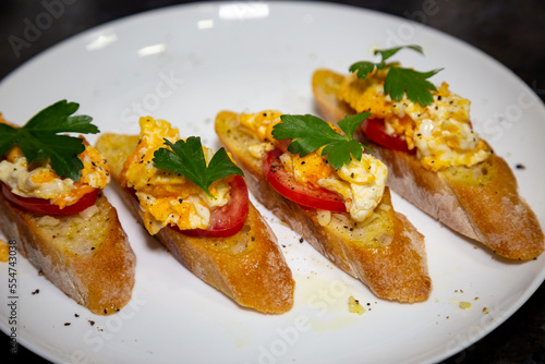 Bread with scrambled egg over ripe tomato and decorated with parsley leaf and black pepper