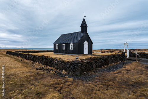 Scenic view of the late-winter landscape at the iconic black church of Búðir (or Budir), surrounded by a natural stone wall, Snæfellsnes peninsula, Iceland