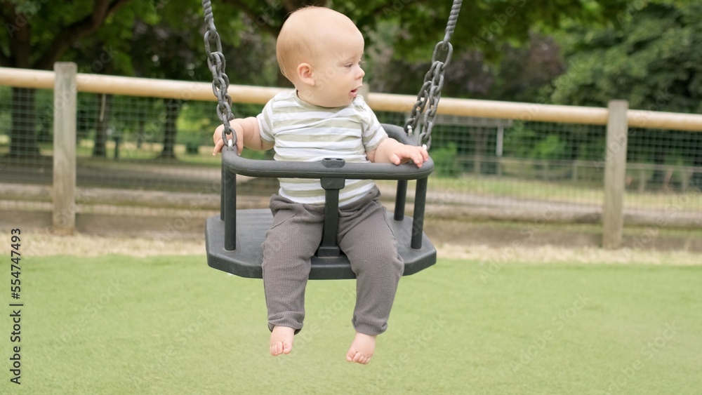 Funny Little Younger Newborn Infant Brother Boy On Swing. Baby Playing On Playground. Summer time outside. Kids Entertainment, Childhood, Child Development, Happy Family Concept