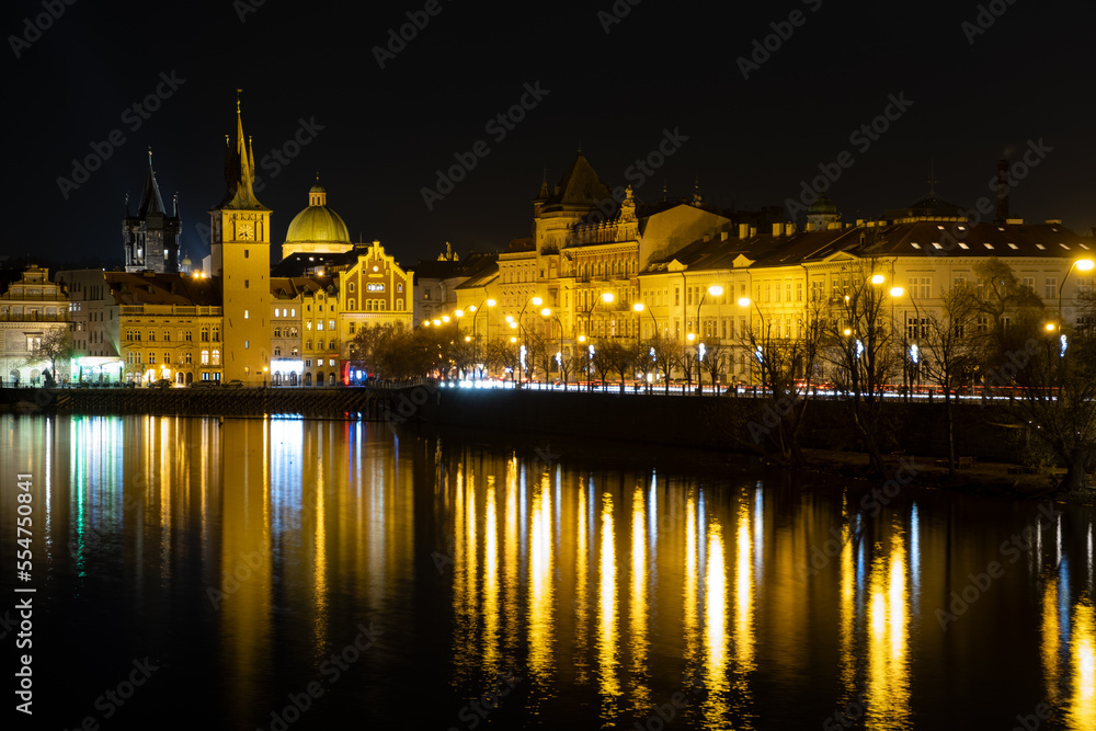 Prague city landscape scenery illuminated river Vltava at night, gothic architecture tower and building with dome in the old town.