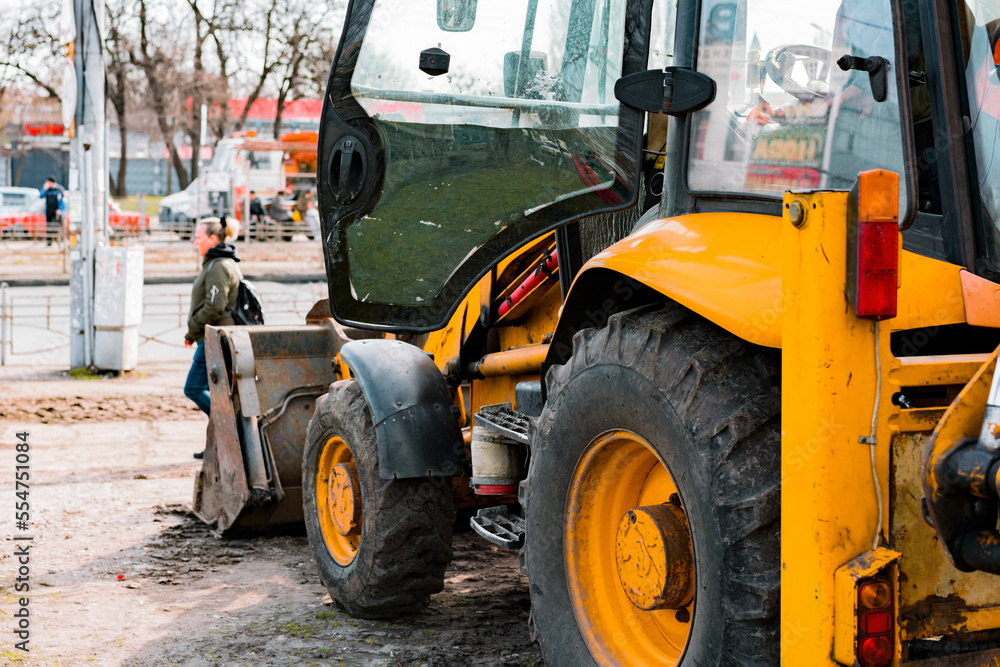 Yellow excavator stands on the ground near a sidewalk. Repair in the city. Preparation. Machine. Municipal work. Backhoe parked and ready for use for road construction on suburban street Yellow excavator stands on the ground near a sidewalk. Repair in the city. Preparation. Machine. Municipal work. Backhoe parked and ready for use for road construction on suburban street