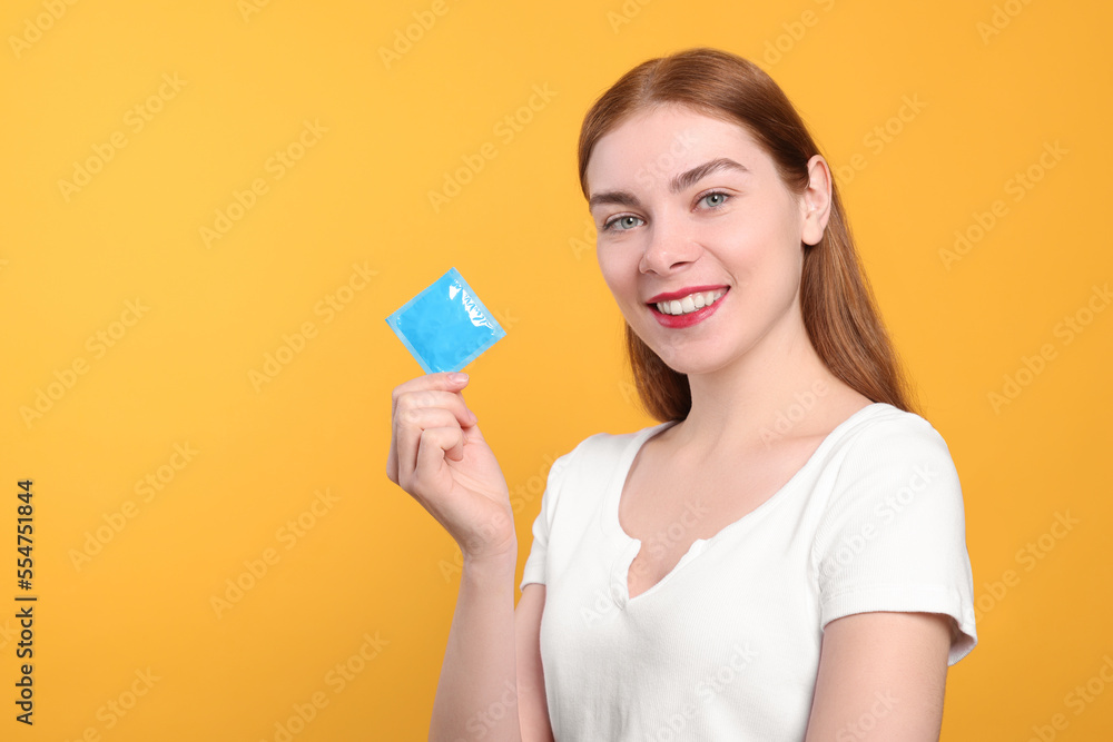 Woman holding condom on yellow background, space for text. Safe sex Woman holding condom on yellow background, space for text. Safe sex