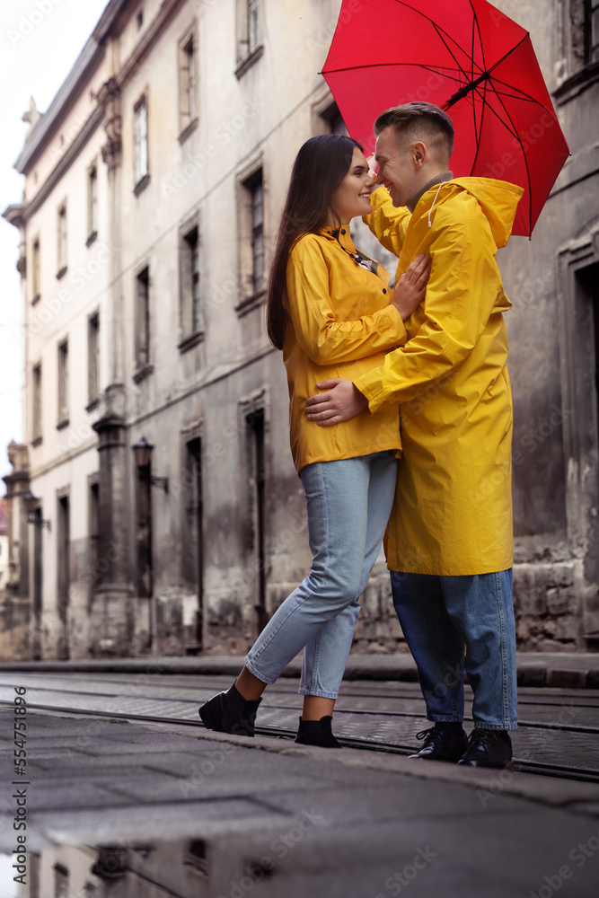 Lovely young couple with red umbrella together on city street