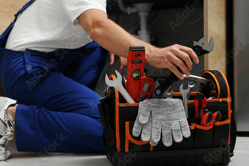 Bild auf Leinwand Professional plumber taking adjustable wrench from tool bag indoors, closeup