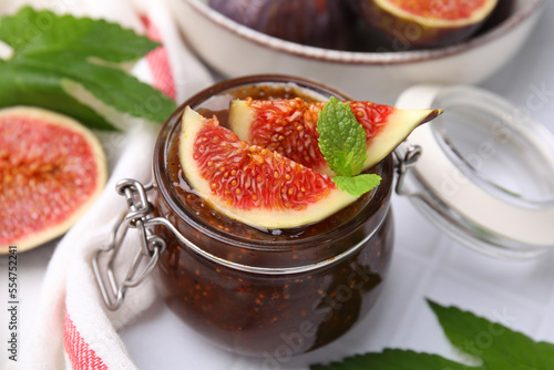Glass jar of tasty sweet fig jam and fruits on table, closeup
