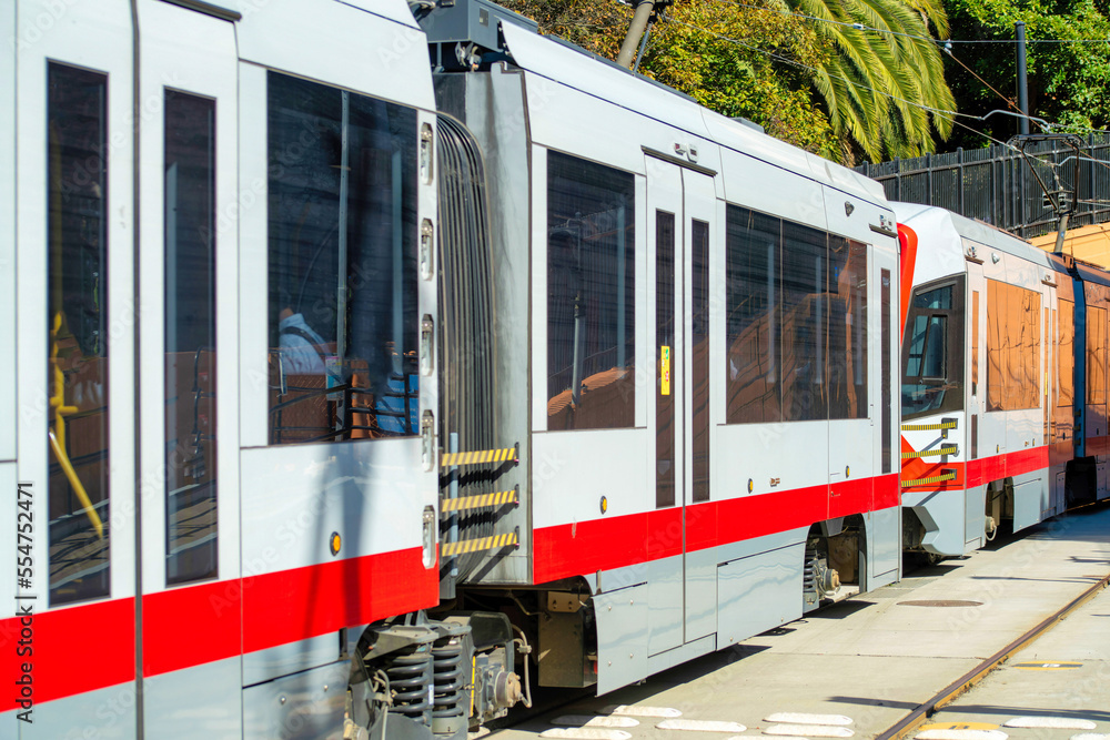 Naklejka premium Tram or downtown train with red and white paint and tinted dark windows with foliage in background and tracks underneath