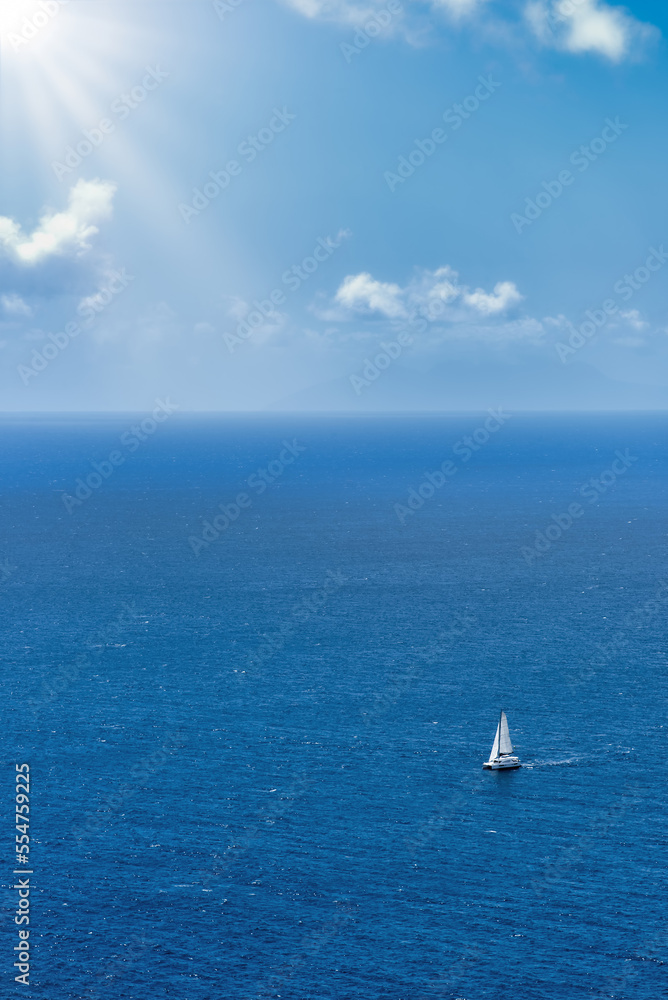 Breathtaking high aerial view of a sailing boat sailing on open sea, beautiful Caribbean ocean, blue skies, white clouds and sunburst