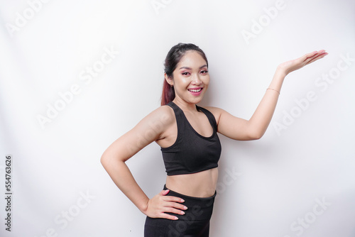 Excited Asian sporty woman wearing sportswear pointing at the copy space on top of her, isolated by white background