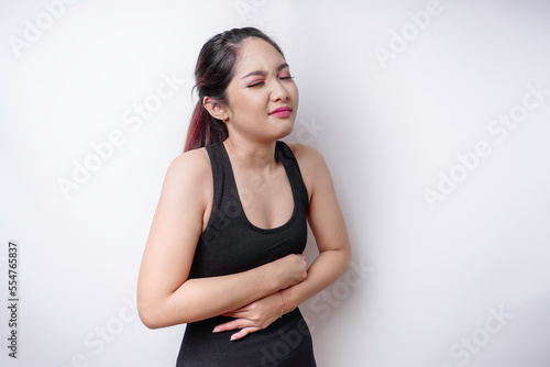 A young unwell sick ill woman wearing sportswear hold hand on stomach suffers pain isolated on white background