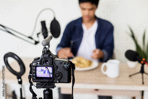Blurry image of Asian young man in casual style prepare for food vlogging using broadcasting equipment.