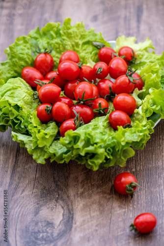 Fresh vegetables: cherry tomatoes and lettuce leaves. Summer harvest. Rustic style food photography. Vertical image on the wooden background