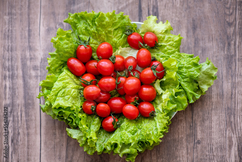 Green lettuce with cherry tomatoes on top on a vegetable plate on dark wooden background. Food preparation. Green eating concept. Top view